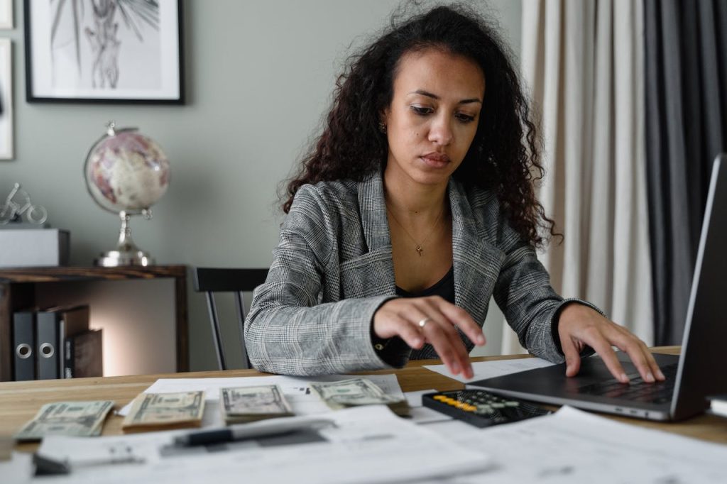 A Woman in Plaid Blazer Using Her Laptop and Mobile Phone for small business finance